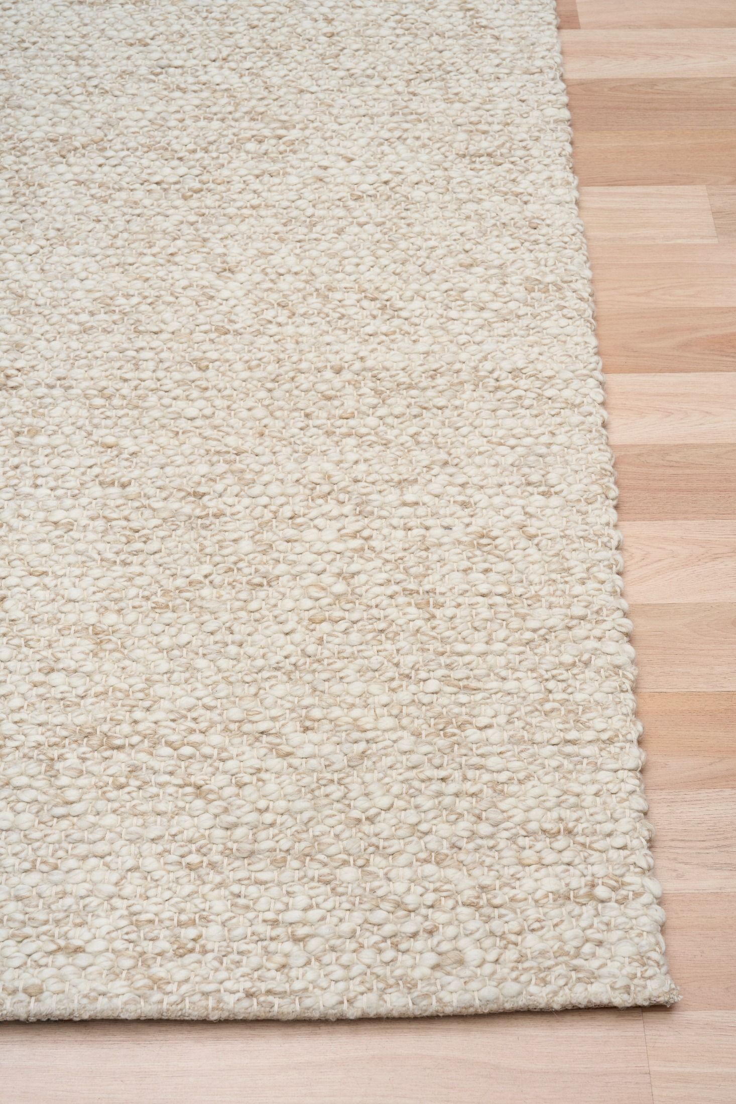 Sahara Wheat Rug – hand woven 100% wool rug in soft neutral tones with a textured finish, available in three sizes, styled for modern and coastal homes. Corner.