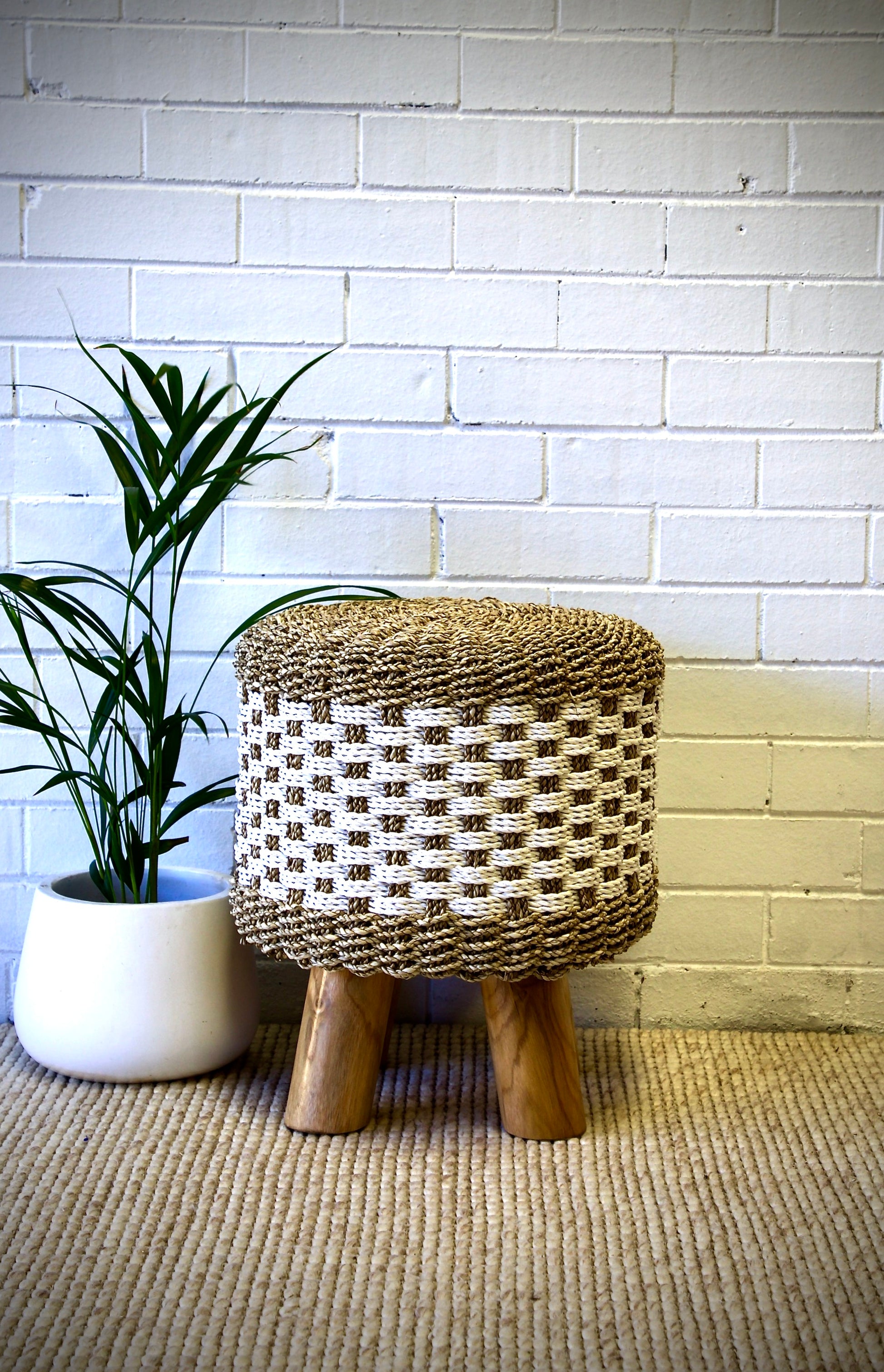 The Saru footstool is crafted from sustainable seagrass and teak legs. Colours natural with white accents. Measures 450 diameter X 500 height. Front Styled.