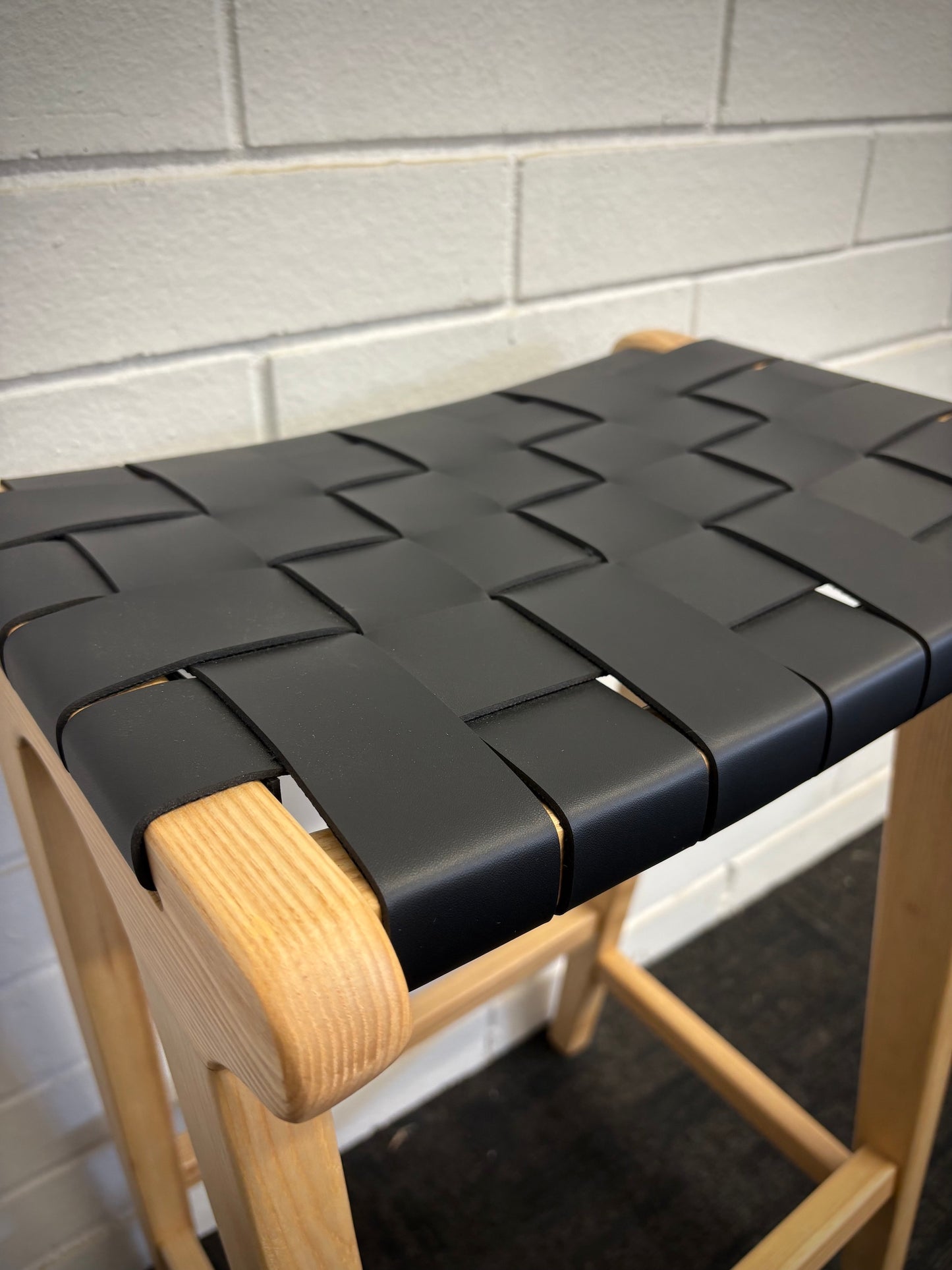 The Thames Barstool, black leather, is designed with a contemporary style. Featuring a sustainable ash frame and a luxurious strapped saddle leather seat. Colour natural frame with black leather. Measures 410 wide X 320 depth X 640 height. Close.