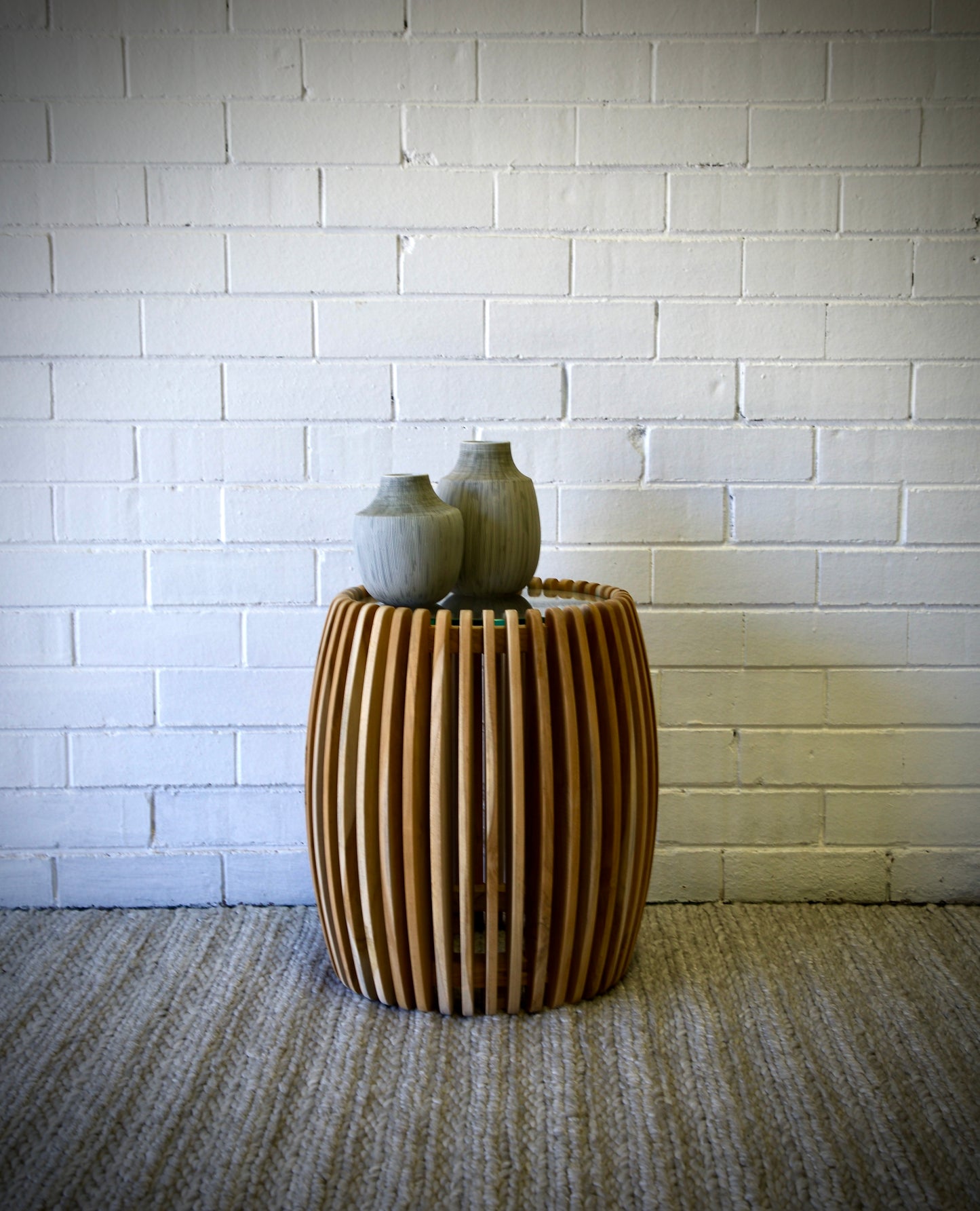 The Tokyo Side Table featuring sustainable teak wood, slated sides and a tempered glass top. Colour natural. Measures 450 diameter X 500 height. Front Styled.