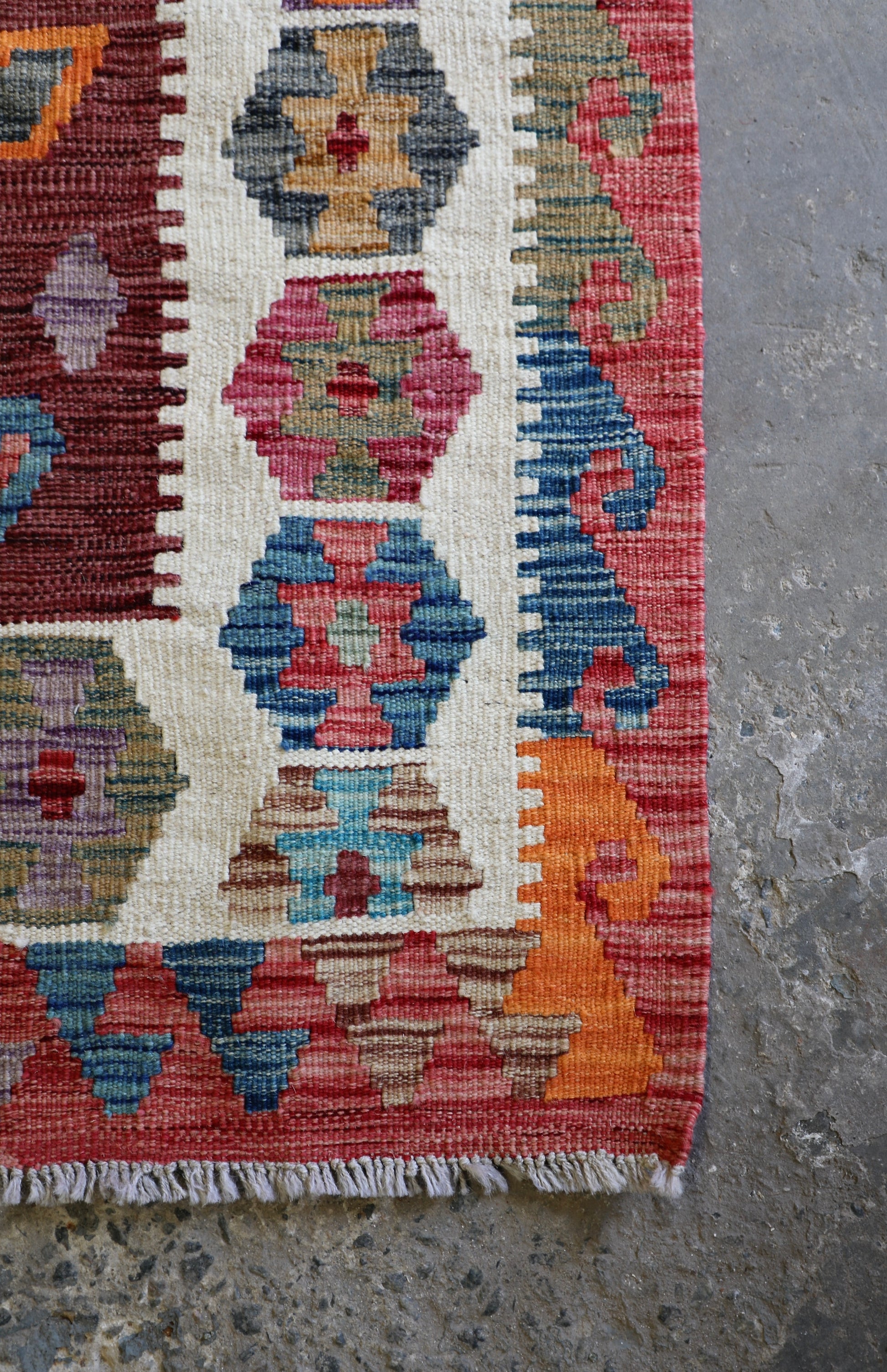 The Afghan Hand Woven Khyber Kilim 122 X 183. Crafted using traditional vegetable dyed wool, and featuring traditional geometric designs. Colours, reds, oranges, browns, creams and teal greens. Size 122 X 183. Corner.