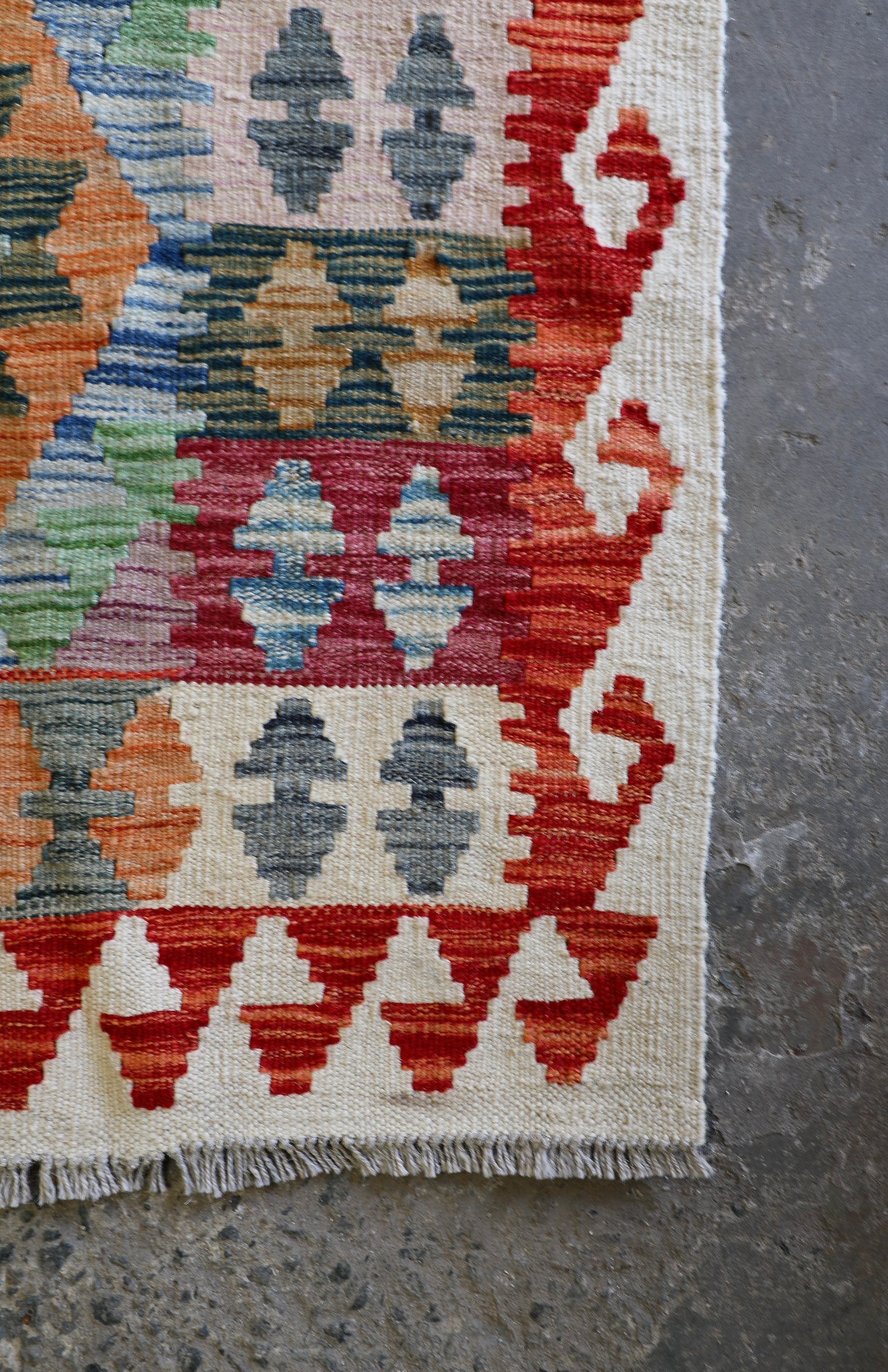 The Afghan Hand Woven Khyber Kilim - 124 X 178. Crafted using traditional vegetable dyed wool, and featuring traditional geometric designs. Colours, creams, oranges, greens and blues. Size 124 X 178. Corner.