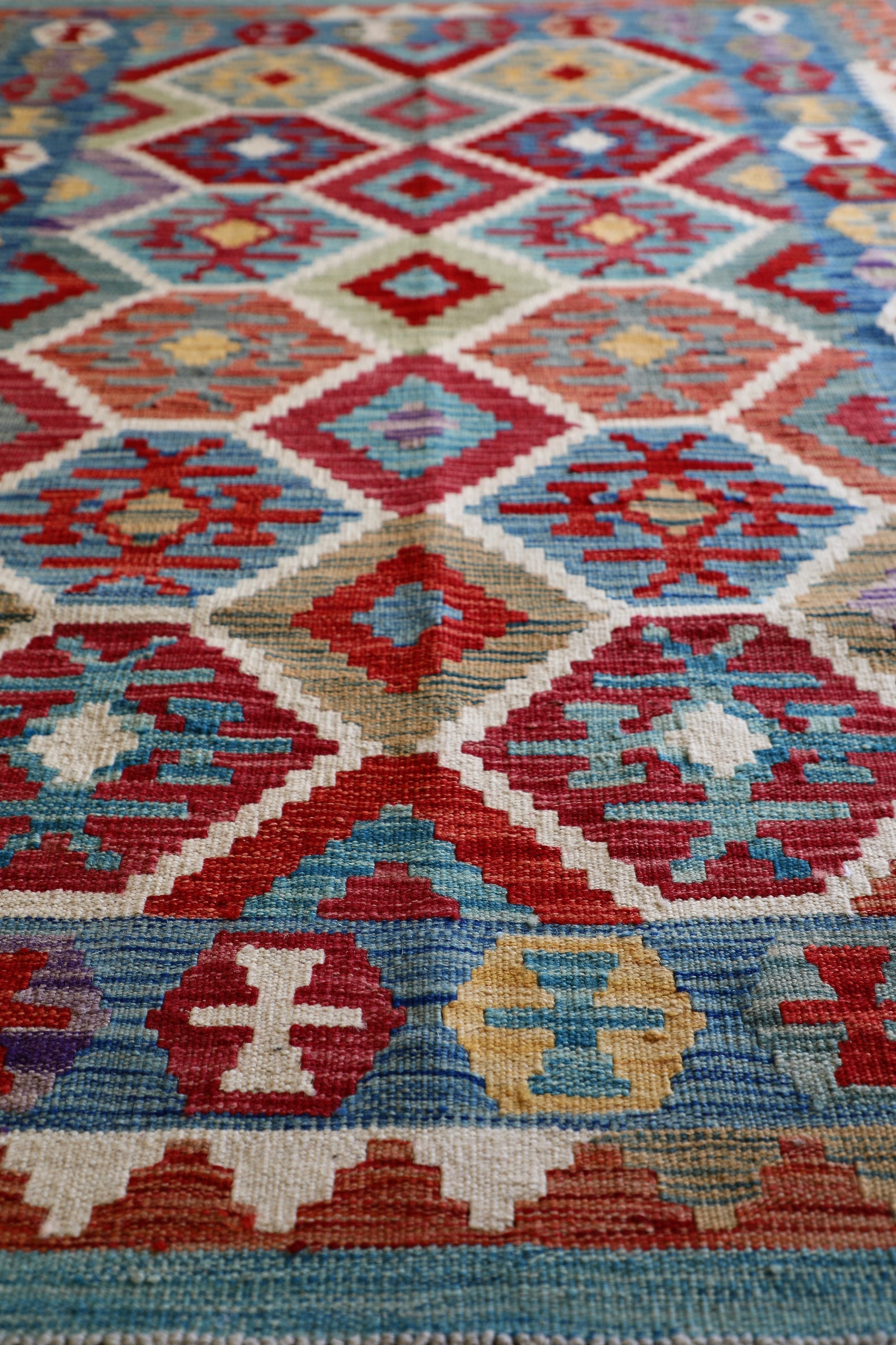 The Afghan Hand Woven Khyber Kilim - 129 X 178.  Crafted using traditional vegetable dyed wool, and featuring traditional geometric designs. Colours, brown, red, blue, cream, teal. Size 129 X 178. Angle.