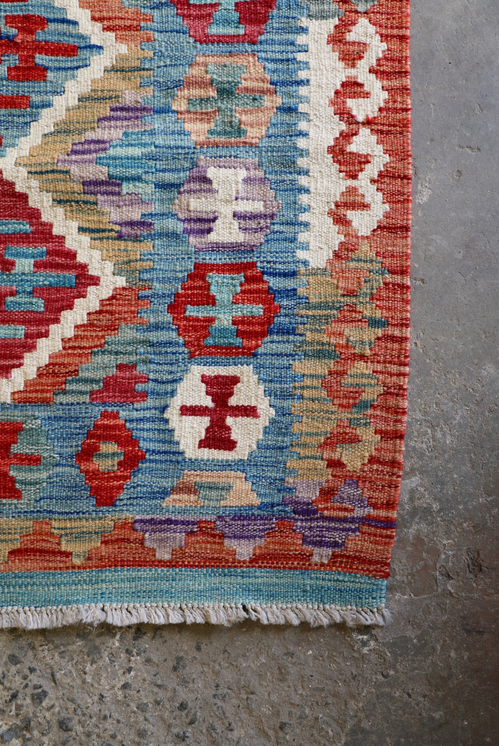 The Afghan Hand Woven Khyber Kilim - 129 X 178.  Crafted using traditional vegetable dyed wool, and featuring traditional geometric designs. Colours, brown, red, blue, cream, teal. Size 129 X 178. Corner.