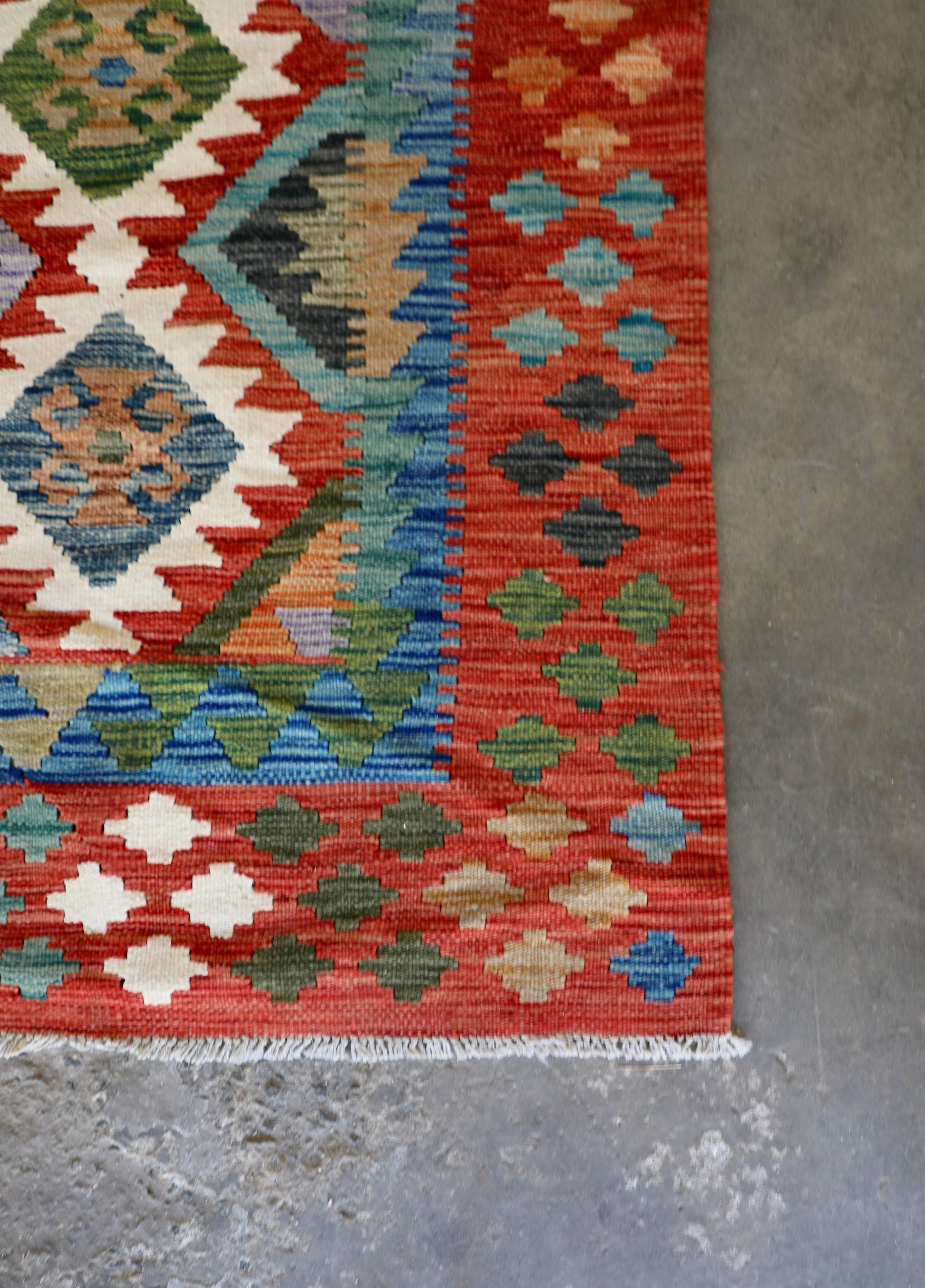 The Afghan Hand Woven Khyber Kilim - 172 X 250. Crafted using traditional vegetable dyed wool, and featuring traditional geometric designs. Colours, cream, reds, greens, blues, oranges. Size 172 X 250. Corner.