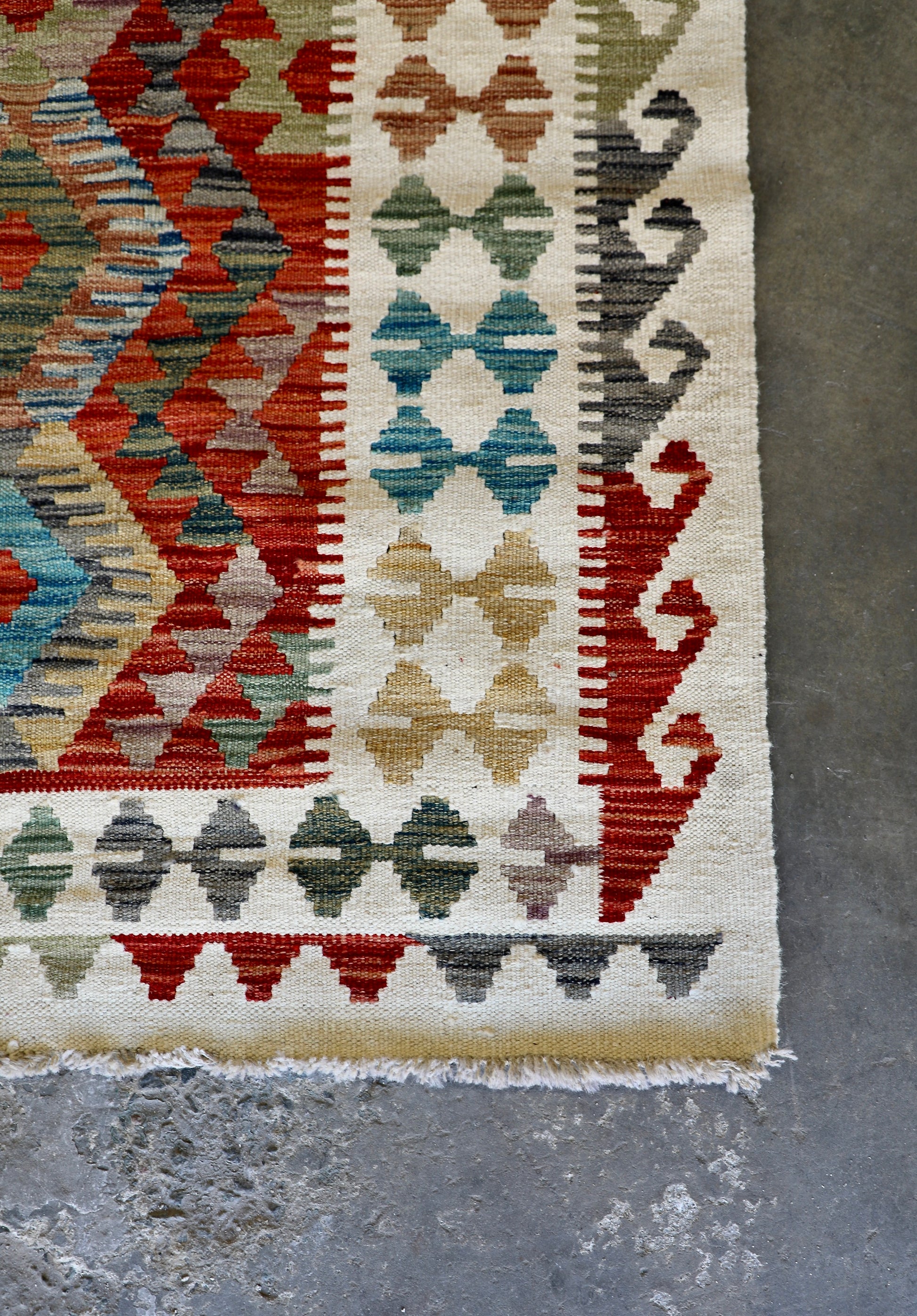 The Afghan Hand Woven Khyber Kilim - 184 X 250. Crafted using traditional vegetable dyed wool, and featuring traditional geometric designs. Colours, cream, reds, oranges, teals, yellows. Size 184 X 250. Corner.