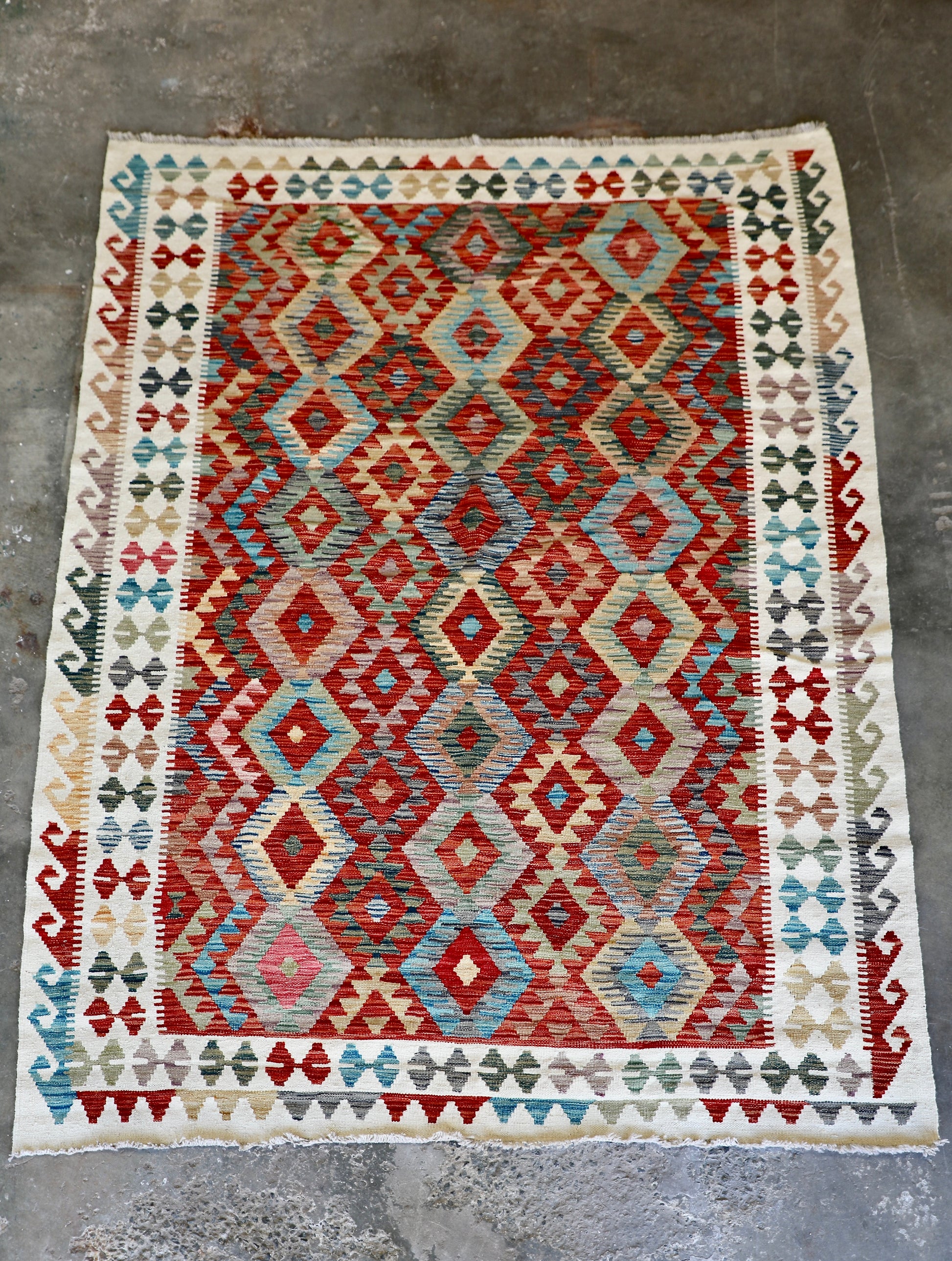 The Afghan Hand Woven Khyber Kilim - 184 X 250. Crafted using traditional vegetable dyed wool, and featuring traditional geometric designs. Colours, cream, reds, oranges, teals, yellows. Size 184 X 250. Front.
