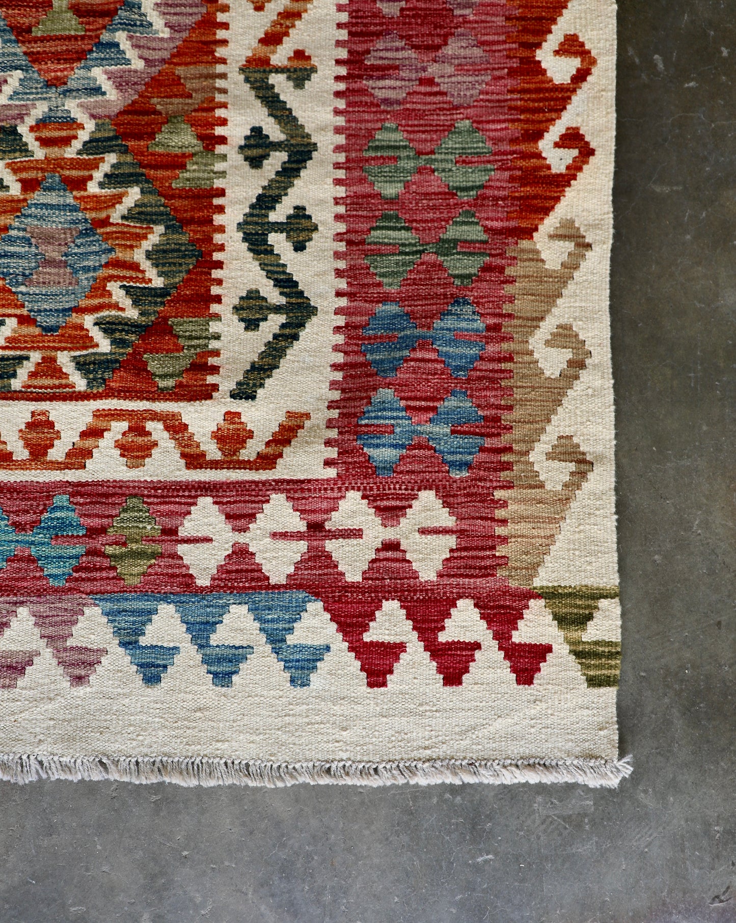 The Afghan Hand Woven Wool Khyber Kilim - 206 X 296.  Crafted using traditional vegetable dyed wool, and featuring traditional geometric designs. Colours, cream, reds, oranges, teals, blues and beiges. Size 206 X 296. Corner.