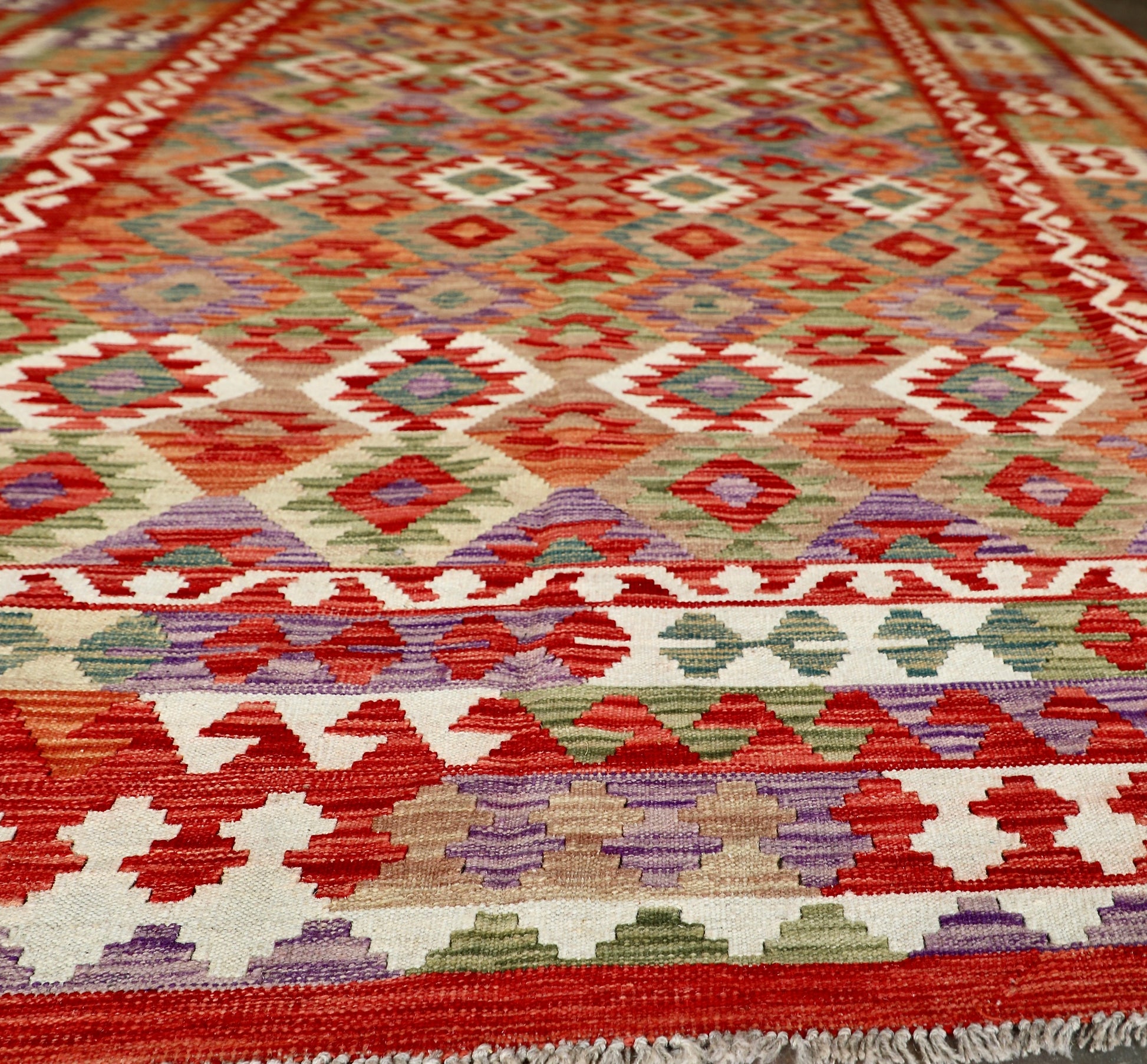 The Afghan Hand Woven Khyber Kilim - 252 X 345. Crafted using traditional vegetable dyed wool, and featuring traditional geometric designs. Colours, Oranges, reds, creams, teals. Size 252 X 345. Angle.