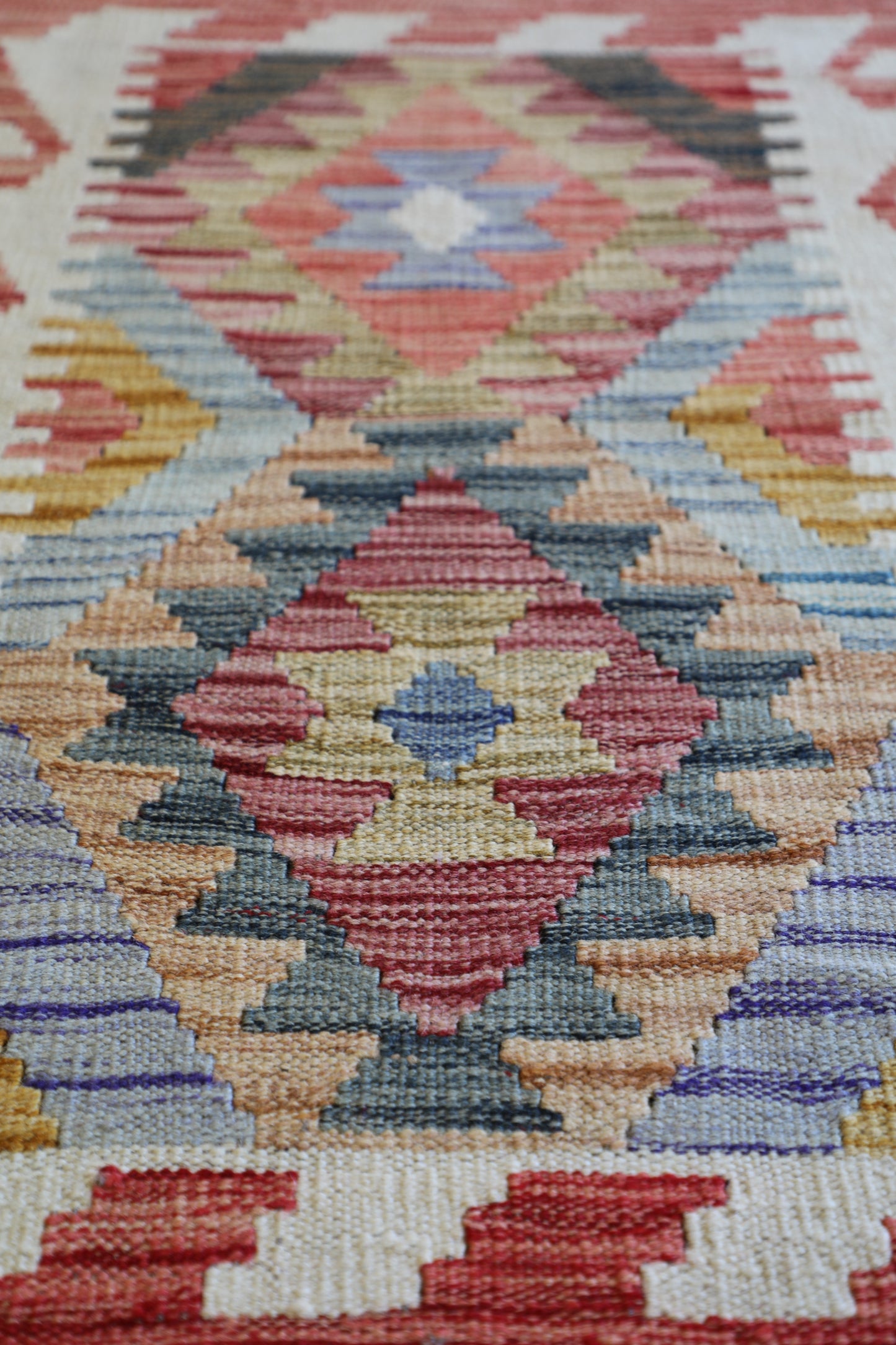 The Afghan Hand Woven Khyber Kilim - 62 X 92. Crafted using traditional vegetable dyed wool, and featuring traditional geometric designs. Colours, oranges, creams, light blues, dark greens. Size 62 X 92. Angle.