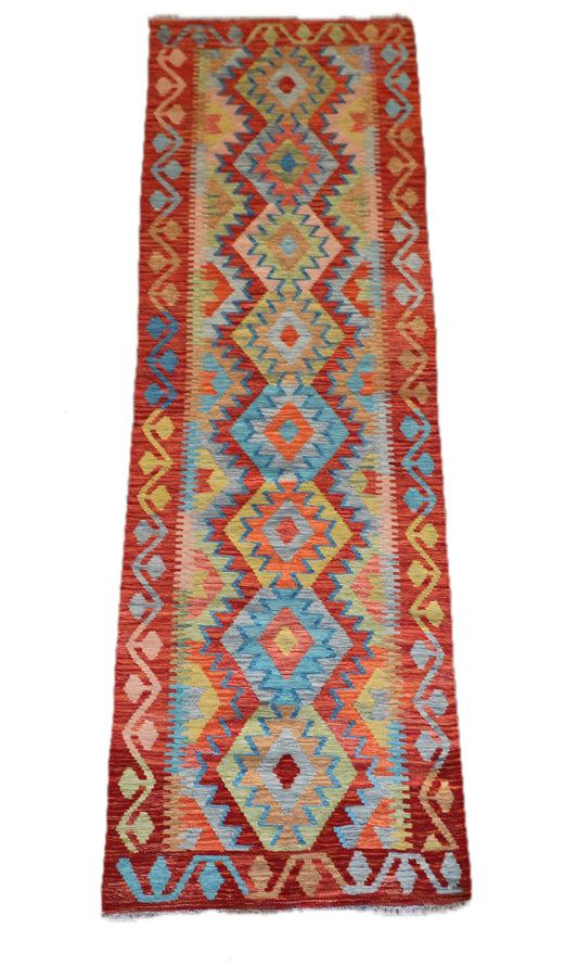 The Afghan Hand Woven Khyber Kilim Runner - 81 X 283. Crafted using traditional vegetable dyed wool, and featuring traditional geometric designs. Colours, reds, oranges, yellows and teal greens. Measures 81 wide X 283 long. Cover.