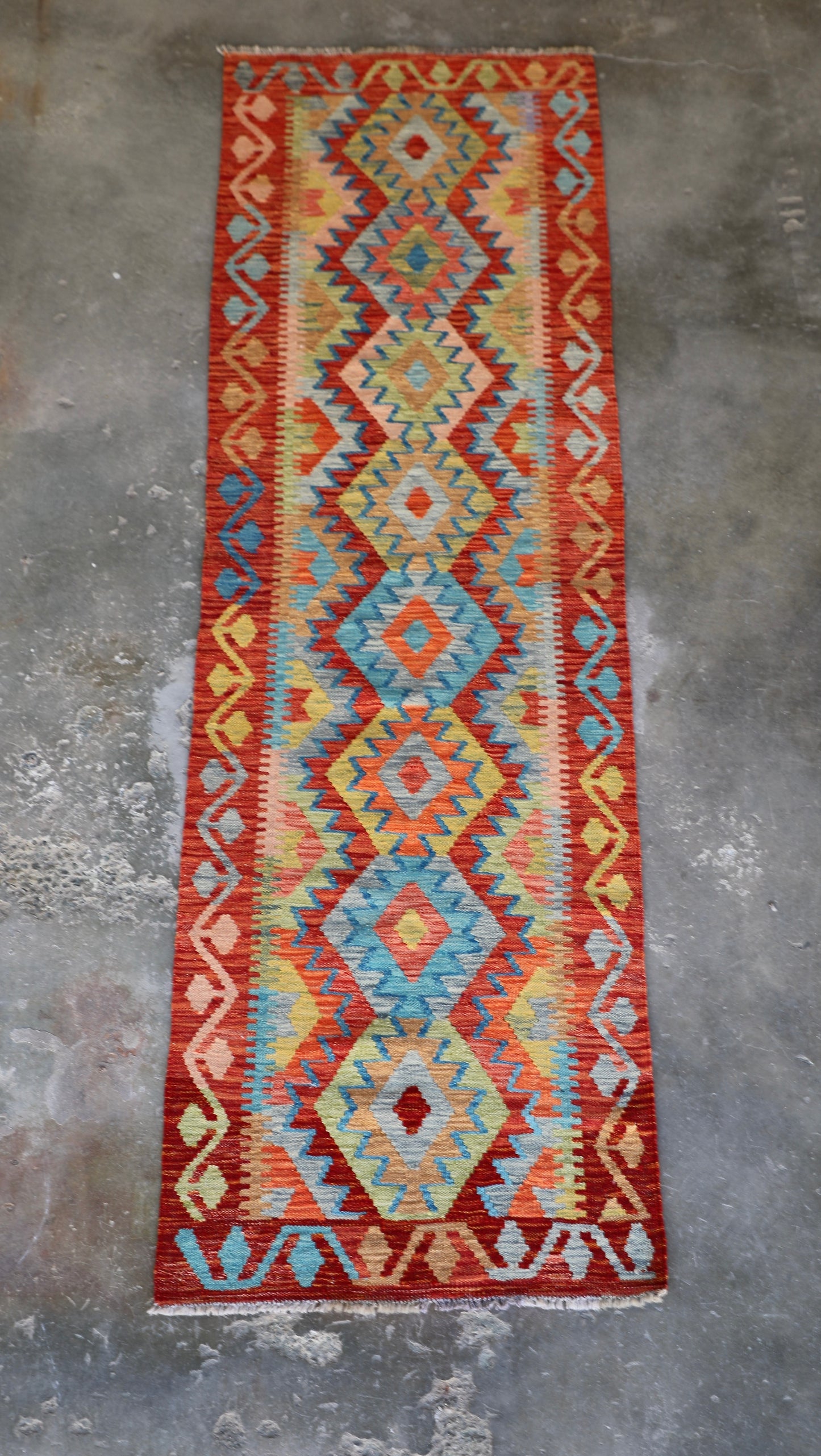 The Afghan Hand Woven Khyber Kilim Runner - 81 X 283. Crafted using traditional vegetable dyed wool, and featuring traditional geometric designs. Colours, reds, oranges, yellows and teal greens. Measures 81 wide X 283 long. Front.