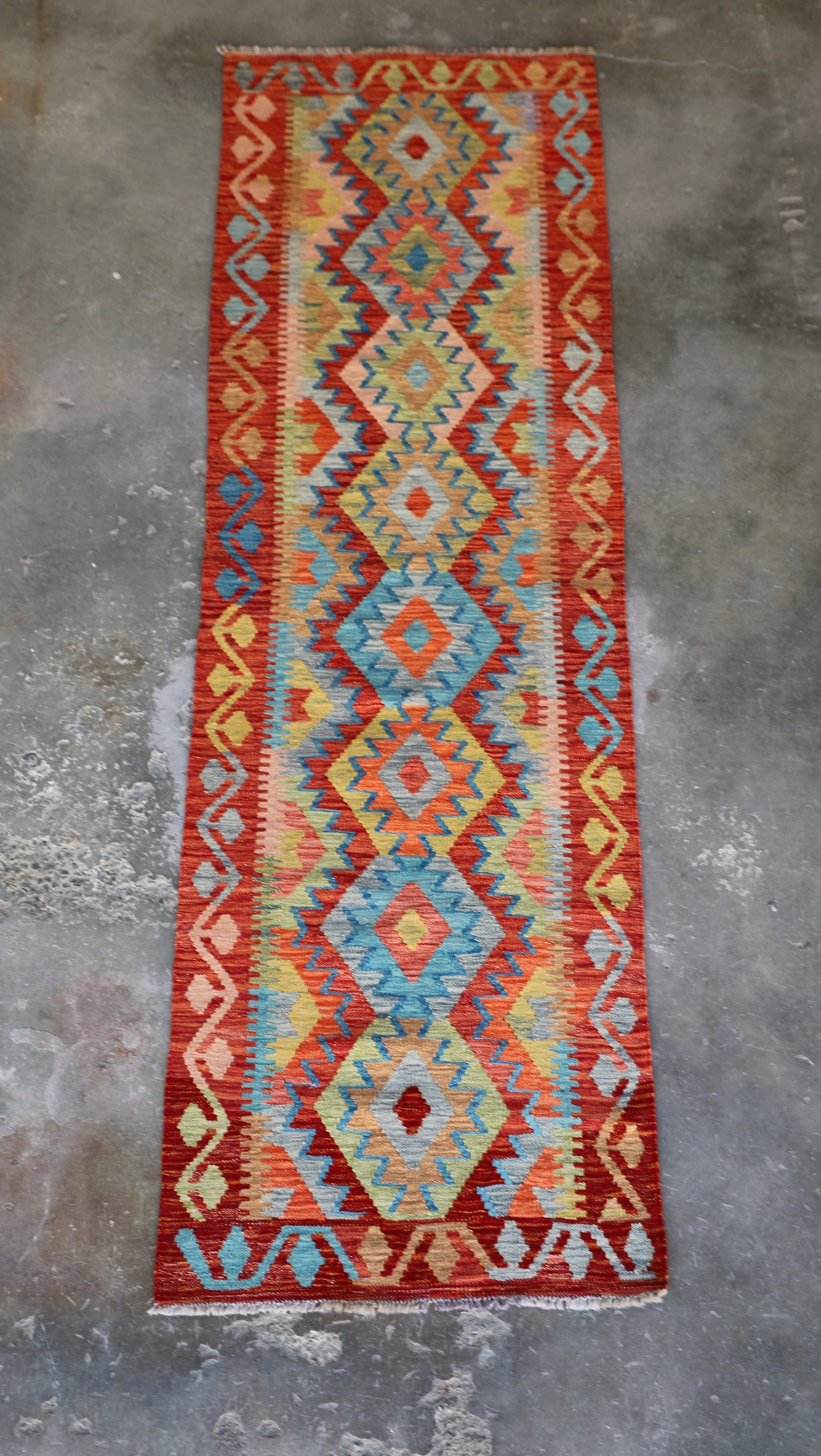 The Afghan Hand Woven Khyber Kilim Runner - 81 X 283. Crafted using traditional vegetable dyed wool, and featuring traditional geometric designs. Colours, reds, oranges, yellows and teal greens. Measures 81 wide X 283 long. Front.