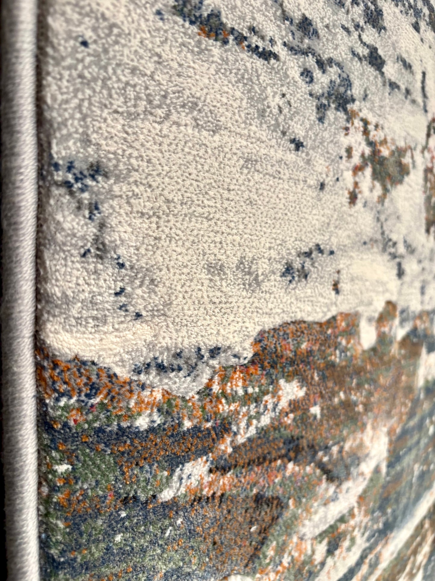 The Zenith Terrain rug. This rug is skilfully crafted from heat-set polypropylene, showcasing a stylish contemporary design. Colours, whites, blues beiges, dark greys. Side Close.